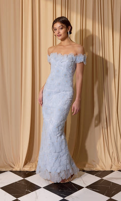 A woman wearing the Long Prom Dress: Eureka EK205 in powder blue stands on a black-and-white tiled floor before beige curtains.