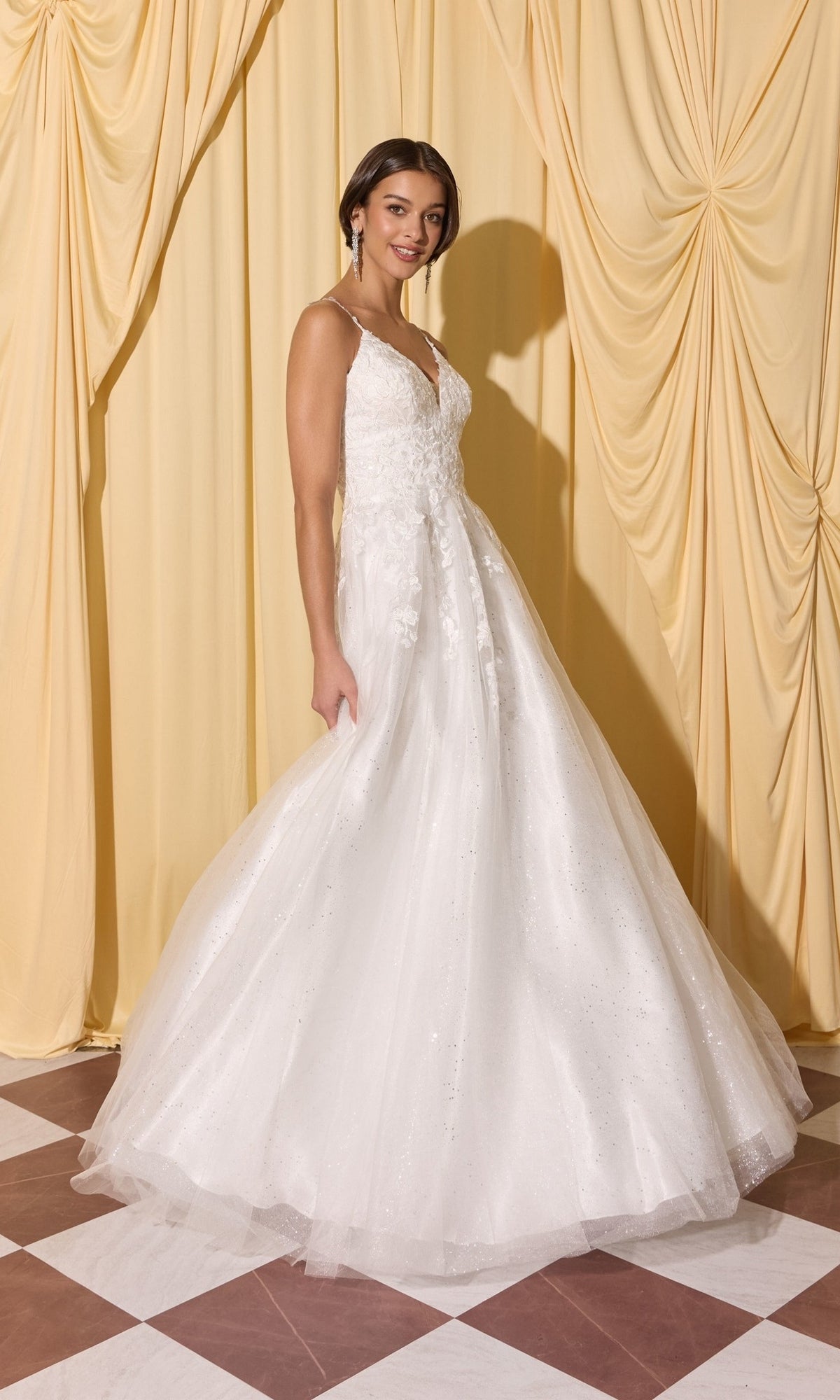 Woman wearing the Long Prom Dress: Eureka EK210, a white sleeveless floor-length gown with lace and 3D floral appliques, on a checkered floor with yellow draped curtains.
