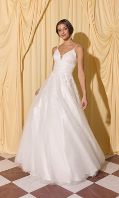 Woman in Long Prom Dress: Eureka EK210, a white sleeveless floor-length gown with 3D floral appliques, stands on a checkered floor before yellow draped curtains.