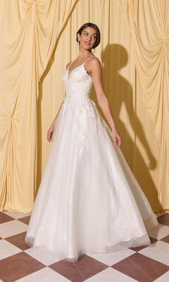 A woman wearing the Long Prom Dress: Eureka EK210, a white sleeveless gown with 3D floral appliques and a tulle skirt, stands on a checkered floor before yellow curtains.