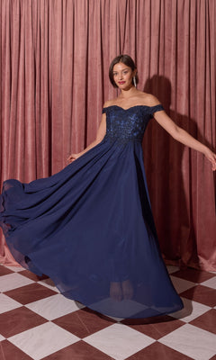 A woman wearing the Long Prom Dress: Eureka EK211 stands on a checkered floor, holding out the skirt; pink curtains hang in the background.