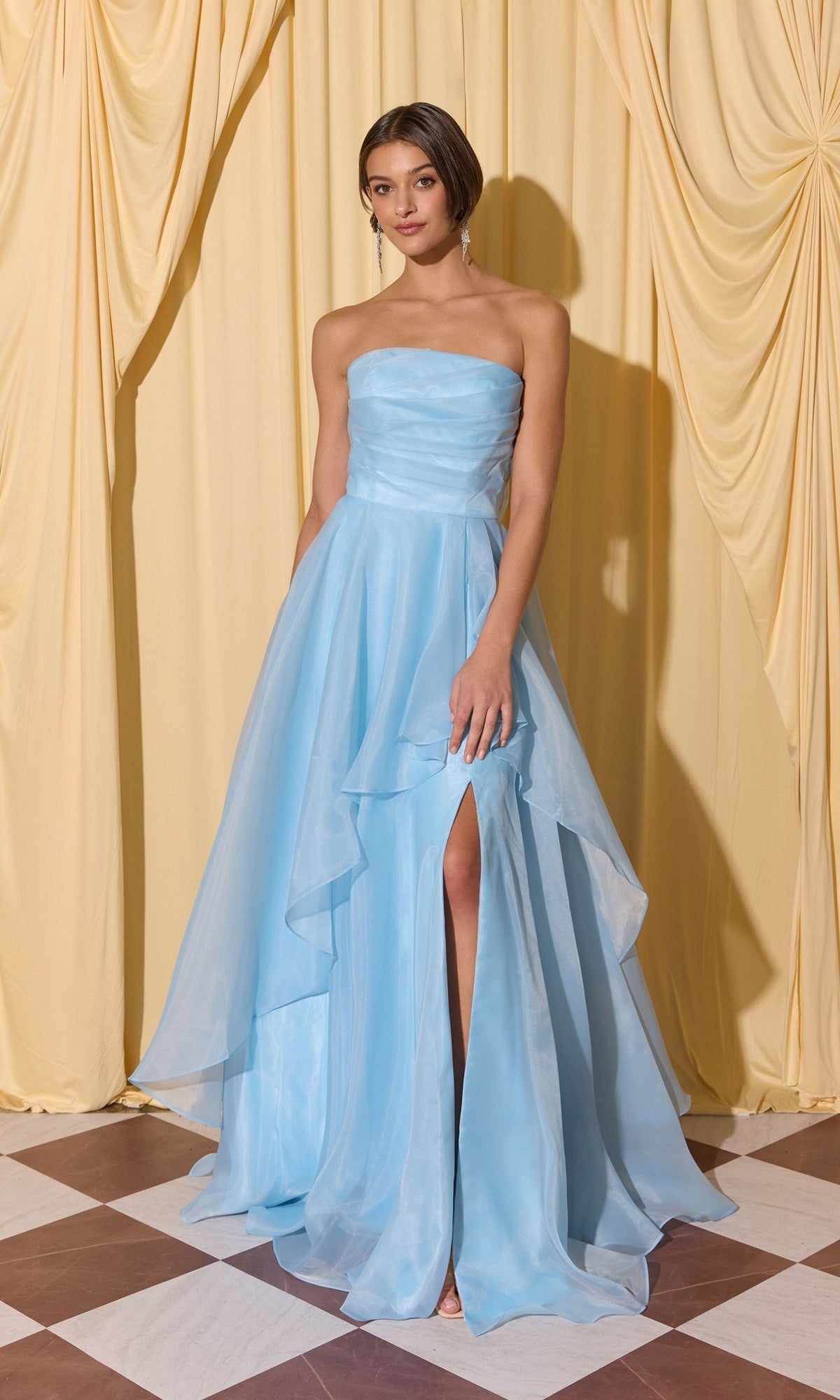 Woman wears Long Prom Dress: Eureka EK216—a strapless light blue gown with high slit and elegant a-line skirt—standing on checkered floor before cream draped curtains.