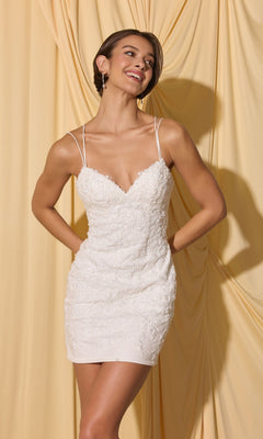 Smiling woman in the Short Homecoming Dress: Eureka EK229, with sequined lace appliques and thin straps, stands before a yellow draped fabric backdrop.