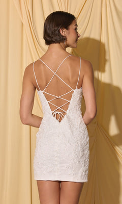 Woman in Short Homecoming Dress: Eureka EK229 with lace-up back and sequined lace appliques, standing before draped beige fabric, facing away from the camera.