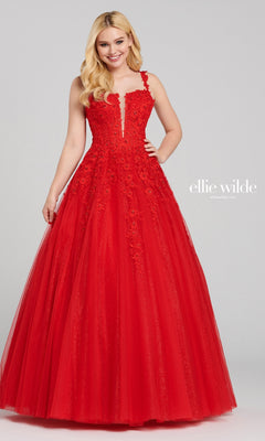 A woman wears the Ellie Wilde EW120014 long glitter prom ball gown, a red sleeveless A-line dress with floral lace details and a sparkling tulle skirt, standing against a plain background.