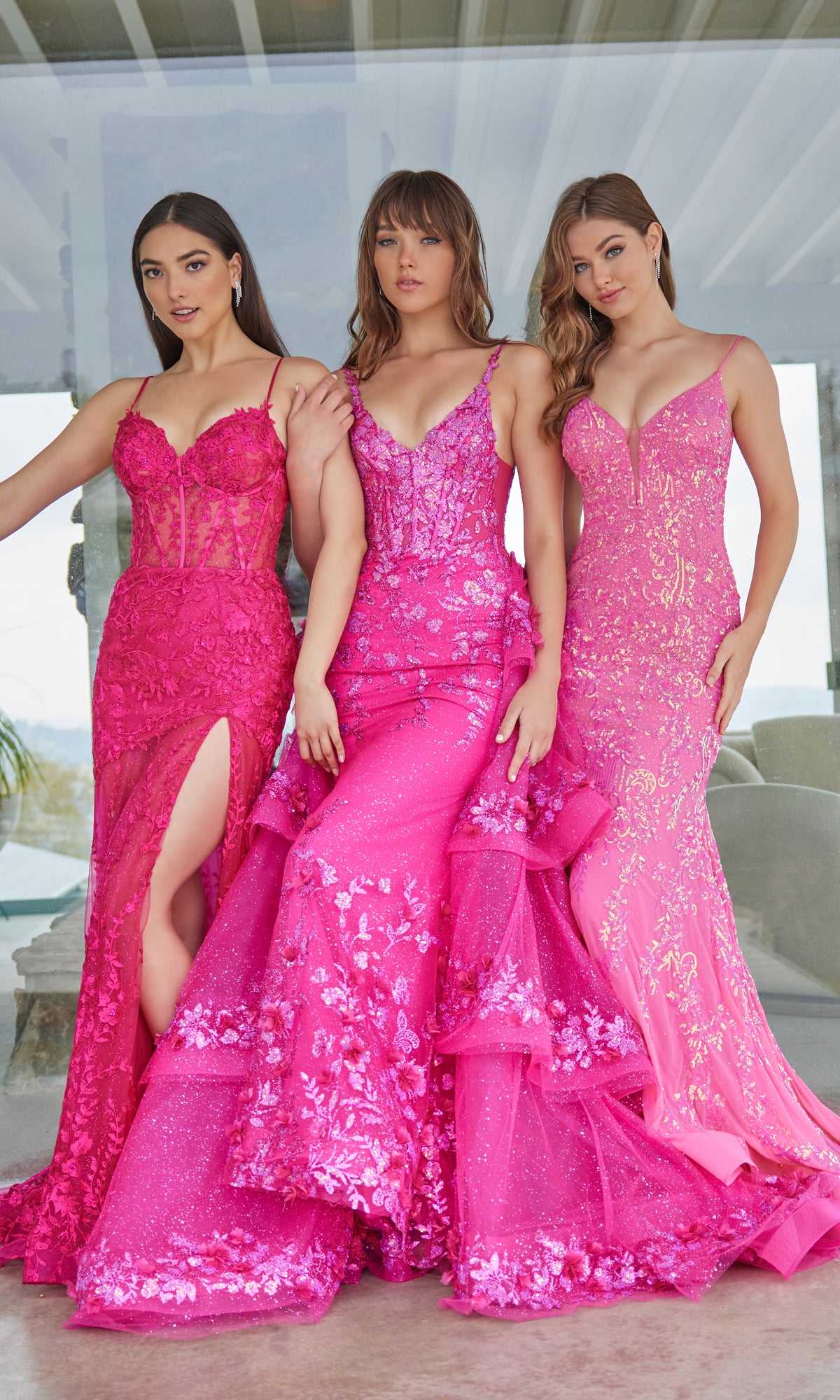 Three women stand side by side wearing bright pink Ellie Wilde evening gowns, including the stunning Ellie Wilde Long Lace Mermaid Prom Dress EW35005 with intricate lace and sequin detailing.