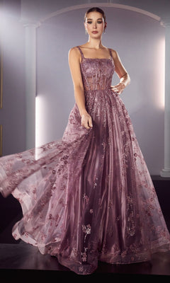 A woman poses in the Long A-Line Glitter-Print Prom Dress J840, a floor-length gown featuring sheer panels and intricate floral detailing, set against a backdrop with arched columns.