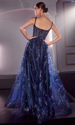 A woman stands with her back to the camera, wearing the Long A-Line Glitter-Print Prom Dress J840 in deep blue with floral embroidery and a sheer overlay, her hair styled in a sleek bun.