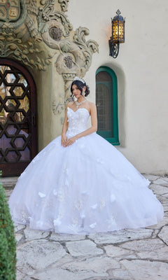A woman wearing the Long Wedding Dress: Juliet JT1495HW in white stands on a stone path before an ornate doorway with a curved, vine-like design and a green-framed window.