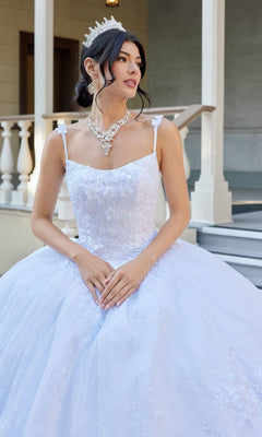 A woman wearing the Long Wedding Dress: Juliet JT1496HW, featuring white floral lace appliques, and a tiara, stands on steps in front of a building with white railings.