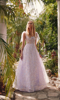 A woman wearing the Lilac Purple Long Lace Prom Dress Juliet JT2439K, featuring a sheer bodice and bow sleeves, stands on a stone path framed by lush greenery and elegant columns.
