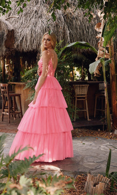 A woman in the Long Prom Dress JT2457H by Juliet stands on a stone path in front of a thatched-roof outdoor bar surrounded by greenery.