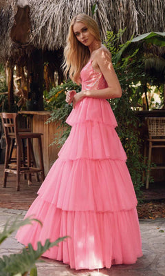 A woman stands outdoors beside wooden chairs and lush greenery, wearing the Long Prom Dress JT2457H by Juliet—a sleeveless fuchsia ball gown with a fitted sequined bodice and tiered skirt.