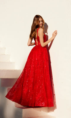 A woman stands near a white wall and staircase, sideways, wearing the Juliet JT2495A long sequin-lace prom dress featuring a sleeveless, floor-length red design with an elegant A-line silhouette.