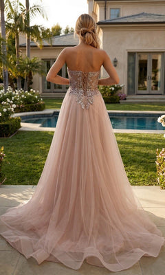 A woman stands outdoors by a pool, facing away in the strapless Flowy Long Tulle Prom Ball Gown: Juliet JT2640G—a blush pink A-line evening dress featuring a floral-beaded corset.