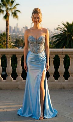 A woman stands outdoors in the Beaded-Corset Strapless Prom Gown Juliet JT2648K, sky blue with a beaded bodice and high slit, against palm trees and a city skyline.