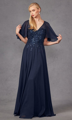 A woman wearing the Long Formal Dress: Juliet JTM14F in navy blue, featuring a floor-length silhouette, sequin-embellished bodice, and sheer flutter sleeves, stands against a plain gray background.