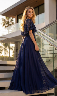 Wearing the Juliet JTM21L long formal dress, a woman stands on outdoor stairs beside a modern building, looking back over her shoulder.