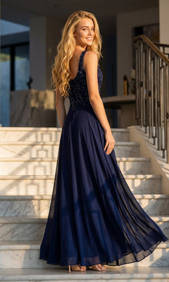 Wearing the Juliet JTM21L long formal dress in navy blue, a woman stands on marble stairs, looking over her shoulder and smiling.