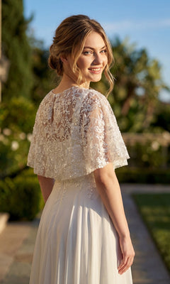 A woman wearing the Juliet JTM21LW long formal dress stands outdoors, smiling over her shoulder with greenery and sunlight in the background.