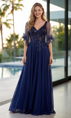 A woman stands by a pool, smiling at the camera, wearing the navy blue Juliet JTM22U long formal dress featuring an embroidered sheer bodice and floral embellishments.