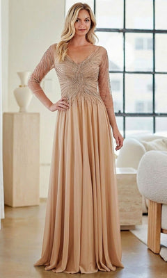 A woman is indoors wearing the gold Long Formal Dress: Amelia Couture KF1501, which features a beaded bodice, sheer embellished sleeves, and an elegant A-line skirt.