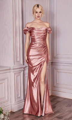A woman poses indoors in the Ruched Long Satin Prom Dress: Ladivine KV1056, an off-the-shoulder rose gold gown with a thigh-high slit and ruched detailing. This affordable formal dress exudes timeless elegance against a pale wall.