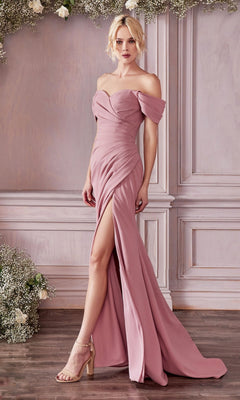 A woman wears the affordable Cold-Shoulder Long Prom Dress with Train KV1057—an off-shoulder, floor-length mauve gown with a thigh-high slit—standing indoors by a paneled wall decorated with flowers.