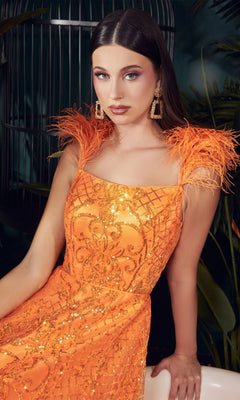 A woman wears the Feathered Neon Orange Long Sequin Prom Dress KV1076 with feathered shoulder straps and statement earrings, posing indoors against a dark background with lush plants.