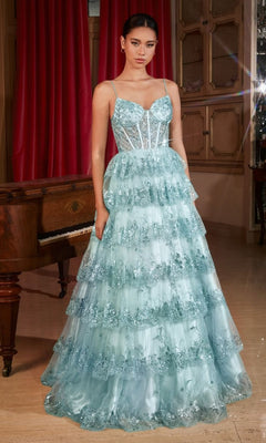 A woman stands indoors in the Sheer-Corset Long Glitter Prom Dress KV1108, a light blue, tiered ruffled gown with sequins and spaghetti straps, posed before a piano and red curtains.