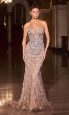 A woman stands in an elegant hallway wearing the Ladivine KV1137 long prom dress in Iridescent/Nude, featuring a fitted, strapless design with sheer fabric and shimmering embellishments.