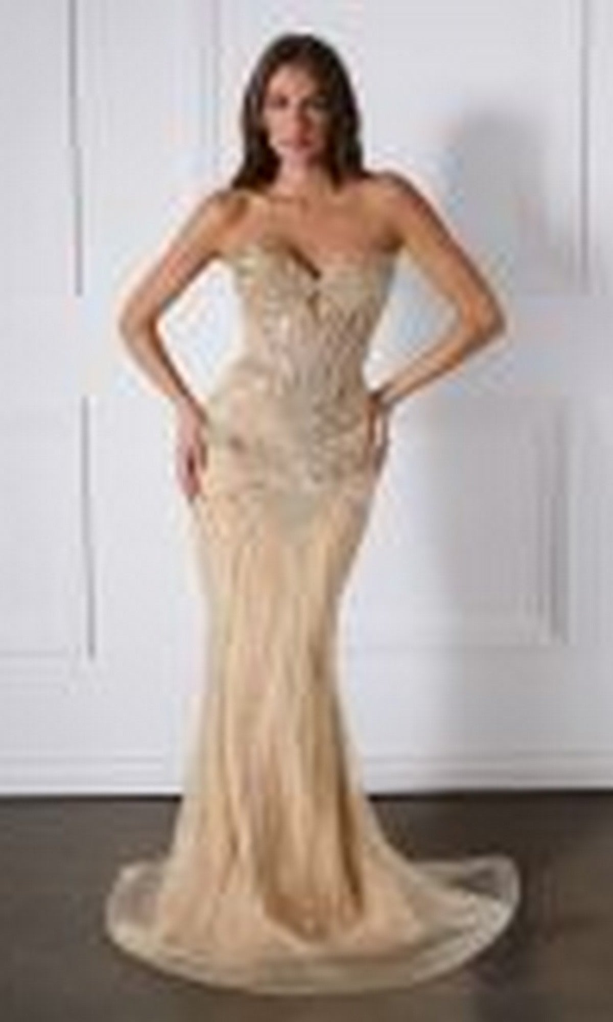 A woman poses in a strapless, form-fitting, floor-length gold Ladivine KV1139 Glitter Prom Dress against a white paneled wall.