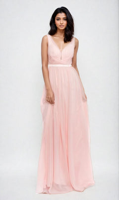 A woman poses against a light background in the Deep V-Back Long A-Line Prom Dress: Chicas C7818, a sleeveless, floor-length gown in light pink with a V-neckline.