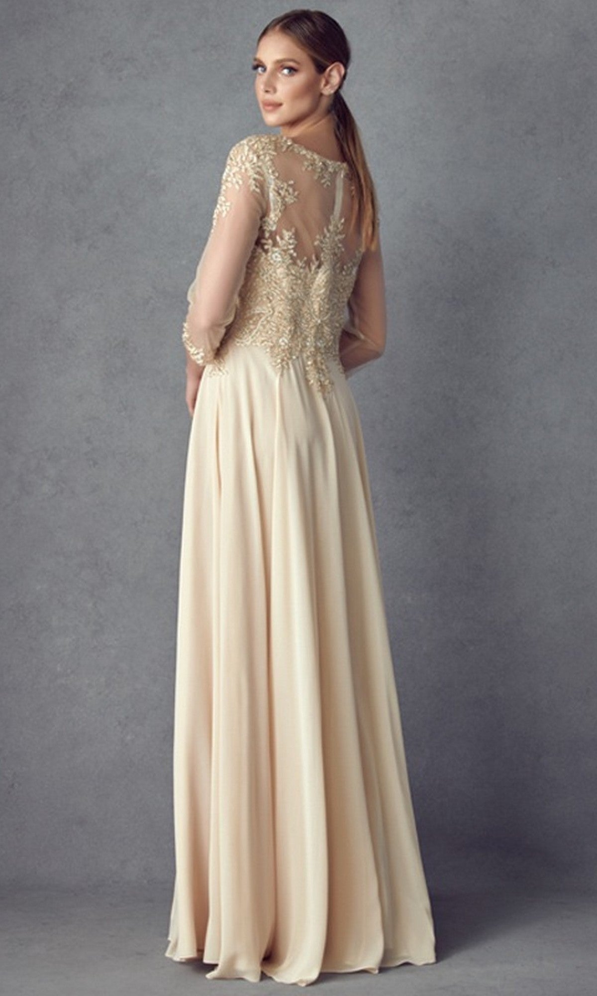 A woman stands against a plain gray background, looking over her shoulder, wearing the Juliet M12 long formal dress—an elegant cream-colored gown with modest sheer lace sleeves and back, delicate floral lace embroidery, and a graceful chiffon A-line skirt.