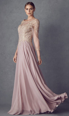 A woman is wearing the Long Formal Dress: Juliet M12 in mauve, featuring a modest design with a chiffon A-line skirt and sheer sleeves. The bodice showcases intricate floral lace embroidery in gold, as she stands against a textured gray background.