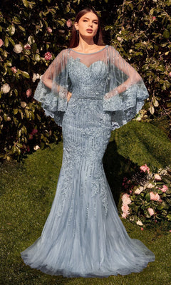 A woman stands on grass in front of flowering bushes, wearing the Cape-Sleeve Beaded Formal Gown by Andrea & Leo (MA105), a fitted light blue dress with lace details and sheer, flowing cape sleeves.
