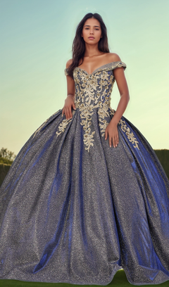 A woman stands outdoors in the Quinceanera Dress 1504 by Dancing Queen, an off-the-shoulder A-line ball gown with gold embroidery, shimmering under a clear sky.