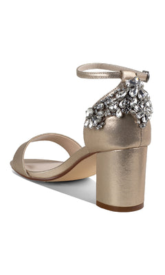 The Olivia Champagne Shimmer Prom Shoes (Touch Ups 4637) are gold heeled sandals with an ankle strap and jeweled heel detail, ideal as champagne prom shoes, shown against a white background.