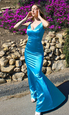 Woman wears the Backless Neon Tight Long Prom Dress SE016 outdoors on a paved path, framed by stone walls and blooming purple flowers.