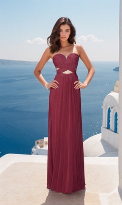Wearing the La Femme Strapless A-Line Designer Prom Dress 22230, a woman stands on a terrace overlooking the blue sea and white buildings, her elegant maroon gown featuring chic cutout details.