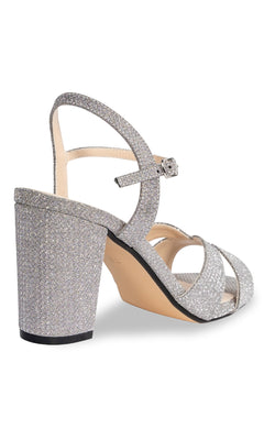 The Riley High-Heel Silver Prom Shoes (Touch Ups 4656) feature a silver glitter finish, ankle strap, and block heel—seen from a back side angle—perfect for your next special event.
