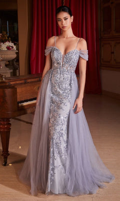 A woman stands indoors by a piano and red curtain, wearing the Ladivine SF009 Tulle Overskirt Long Formal Dress—a floor-length, silver-blue gown with embroidered lace and sheer off-the-shoulder sleeves.