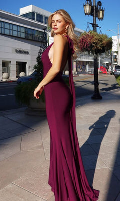 A woman in the Astee T505 Long Prom Dress—sleeveless, floor-length maroon halter style with form-fitting stretch fabric—stands by a lamppost near modern city buildings on a sunny day.