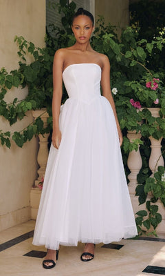 Woman in a white strapless long dress standing in front of greenery