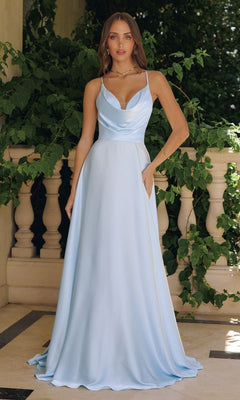 A woman stands outdoors in a Strappy Open-Back Long Prom Gown: Amoris T714, surrounded by green foliage and stone railings.
