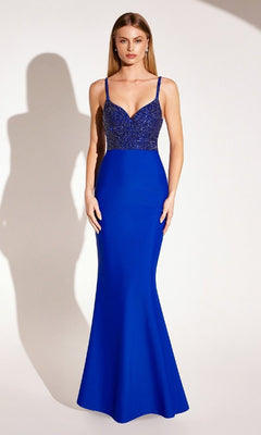 A woman stands against a plain light background wearing the Amoris T9002 Beaded-Bodice Long Prom Dress, a royal blue, floor-length mermaid gown with thin straps.