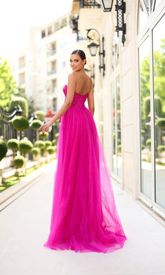 A woman wearing the One-Shoulder Glitter Prom Gown: Tina Holly TK554 stands outdoors on a sunlit walkway, looking back over her shoulder.