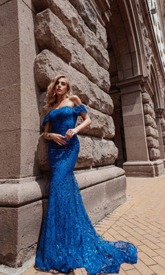Woman wearing the Long Glitter-Lace Prom Dress: Tina Holly TW024, featuring off-the-shoulder sequin details, stands by a stone building with elegant arched architecture.