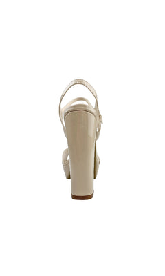 The Whitta Open-Toe Nude Prom Shoes (Dyeables 55817) feature beige patent leather, an ankle strap, open-toe design, and sturdy block heels, shown from the back.