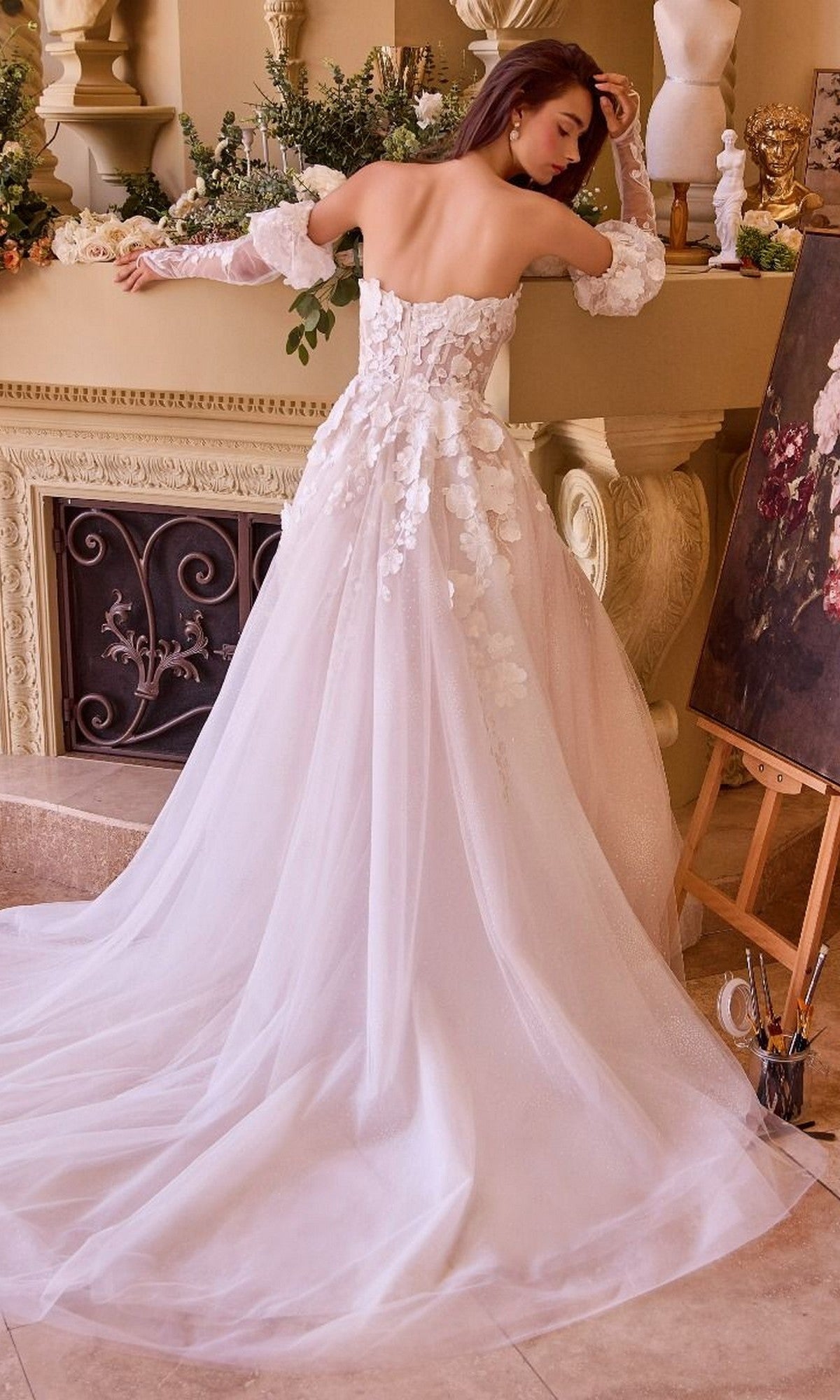 A woman in a strapless Andrea and Leo WL017 long wedding dress stands with her back to the camera in an elegant, art-filled room with supplies and sculptures.